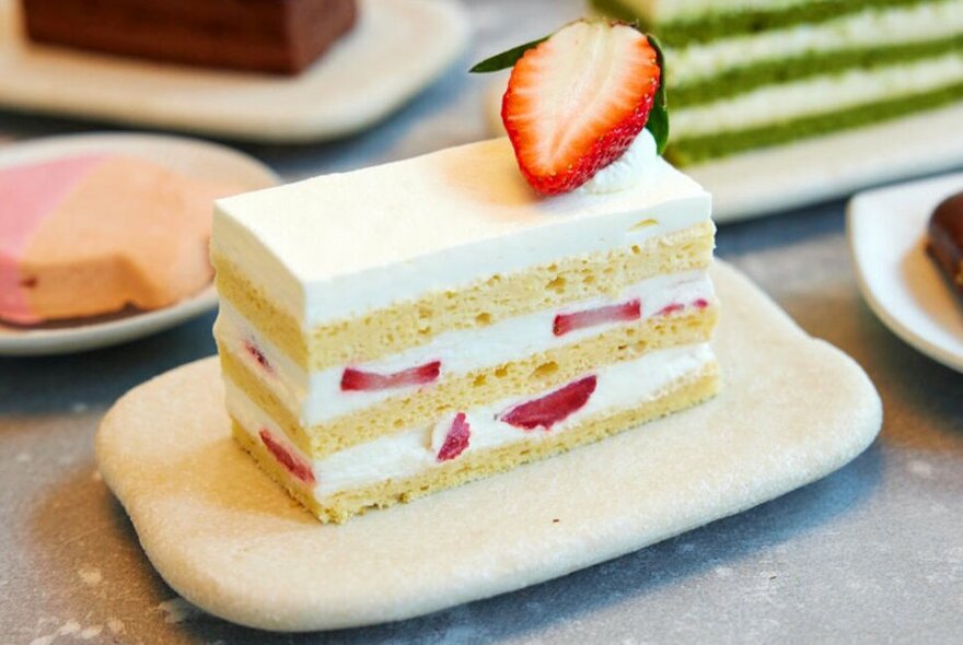 A rectangular slice of multi-layer sponge cake with cream and strawberries