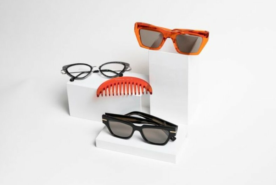 Three pairs of sunglasses and a comb sitting on a white display
