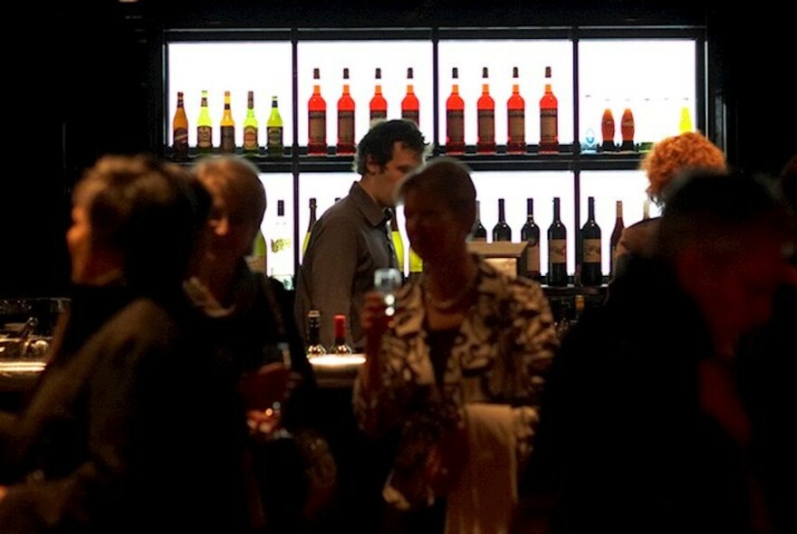 Theatre customers being served at a bar with a backlit display of bottles.