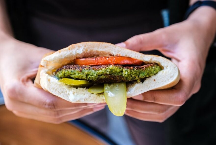 A pita filled with tomato, pickles and a falafel burger. 
