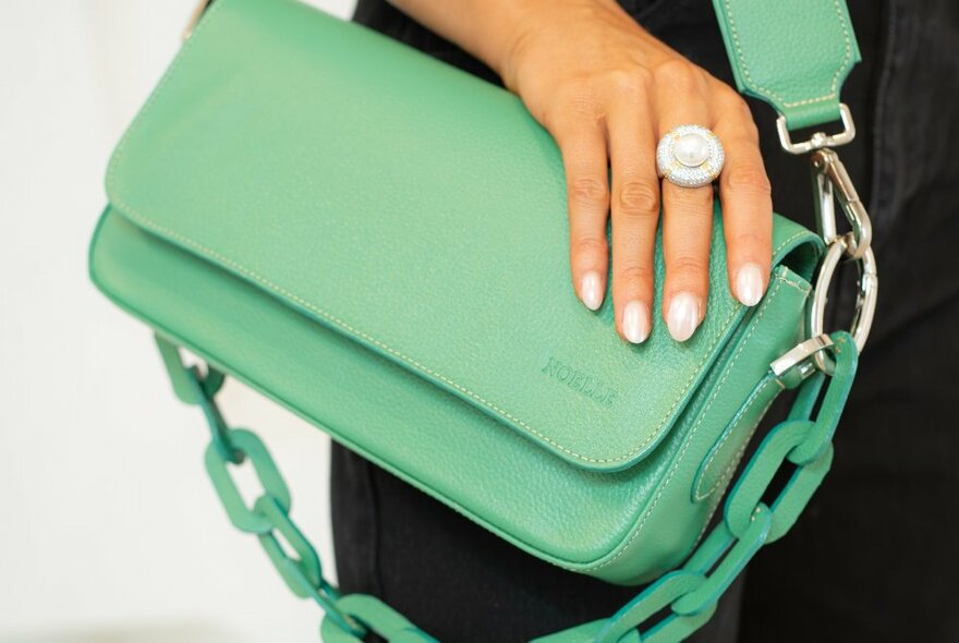 A hand resting on a pale green leather handbag.