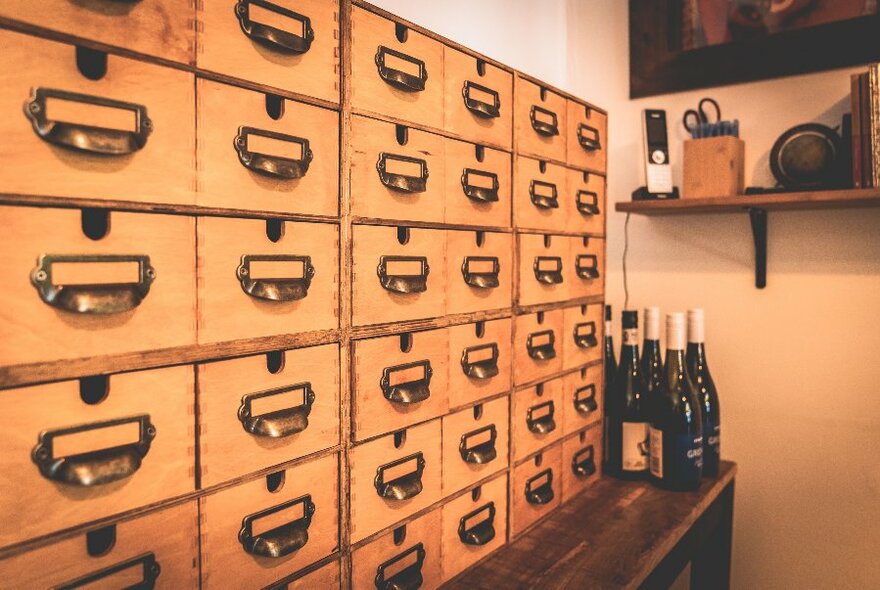 Bottles of wine on a table next to wooden filing drawers.