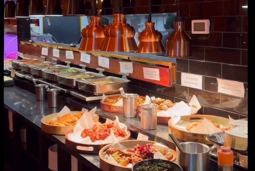 A stainless steel food service area featuring assorted large platters of food on trays and in bowls.