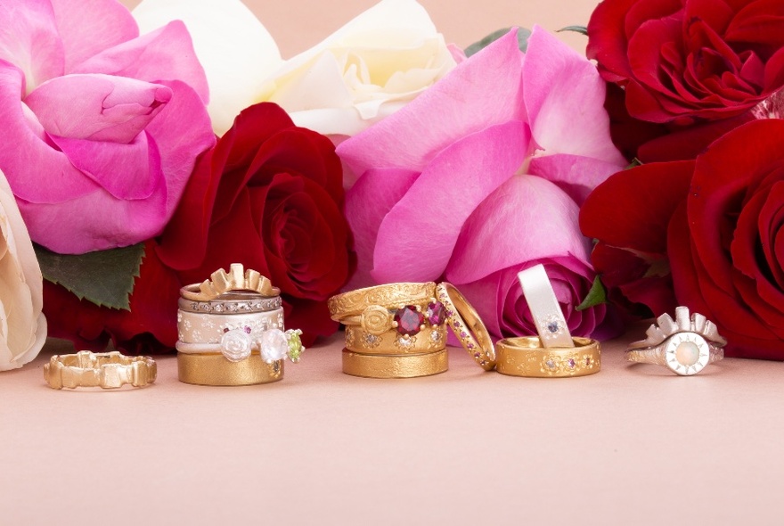 Row of rings, piled on one another, resting against red and pink roses.