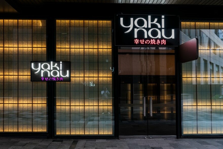 The external shopfront of Yakinau Izakaya Japanese Restaurant, with paper screen-inspired windows and a white neon sign that says yaki nau.