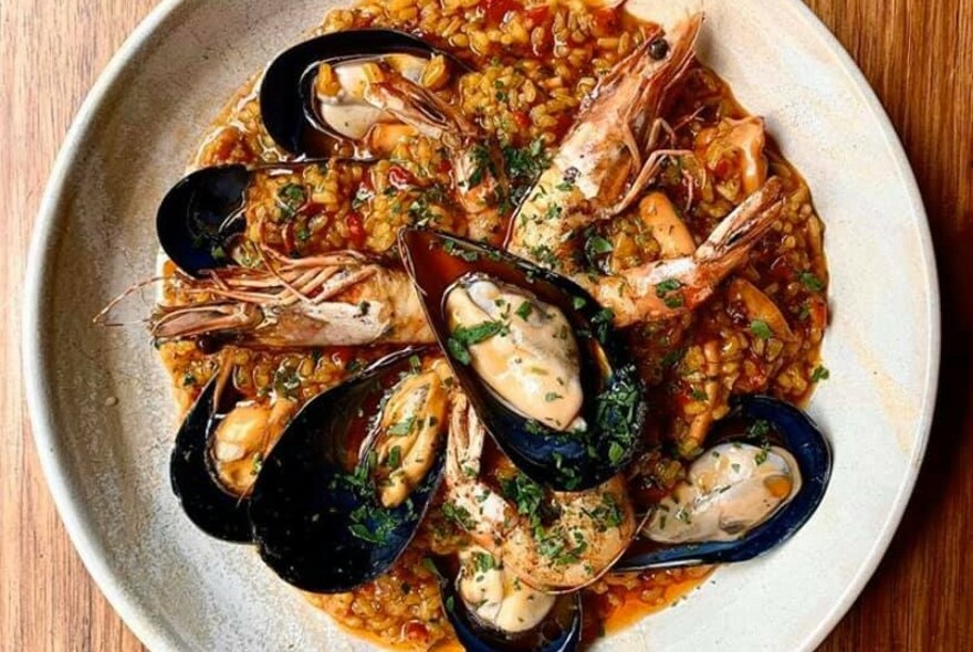 Round dish of paella topped with prawns and mussels.