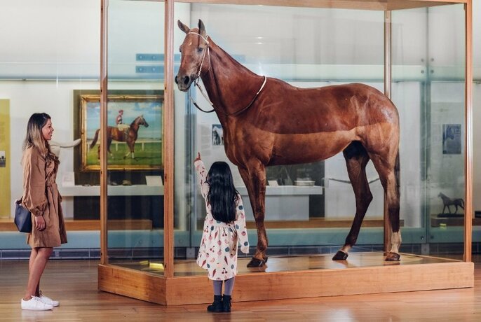 Woman and girl standing looking at the racehorse Pharlap on display inside a glass exhibition case.