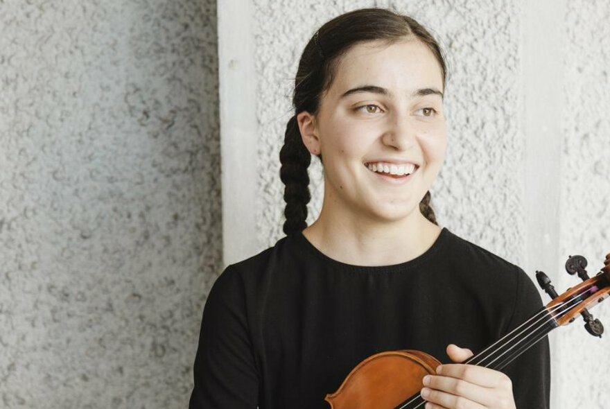 Violinist Louise Turnbull, holding her violin, wearing black with hair in plaits.