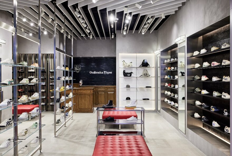 Onitsuka Tiger shoes on display in an industrial-style store with a red bench seat in the middle.