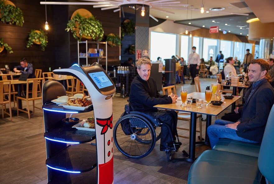 Diners in a dumpling restaurant with a robot waiter delivering food.