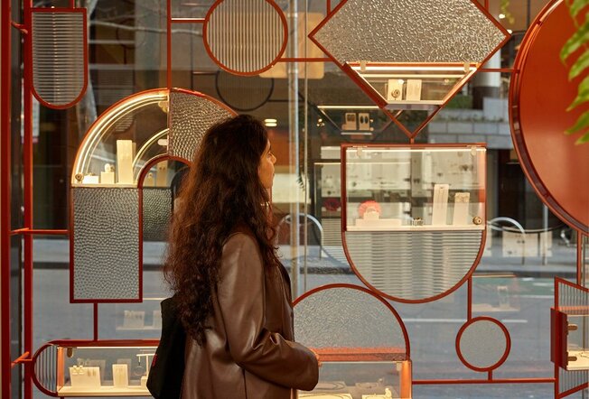 A woman browsing a jewellery display in a geometric window of a boutique.