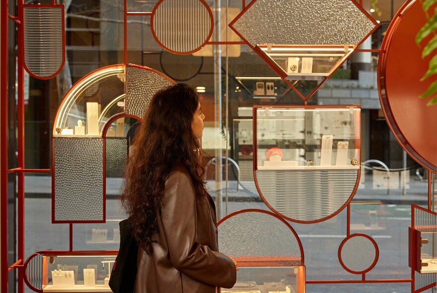 A woman browsing a jewellery display in a geometric window of a boutique.