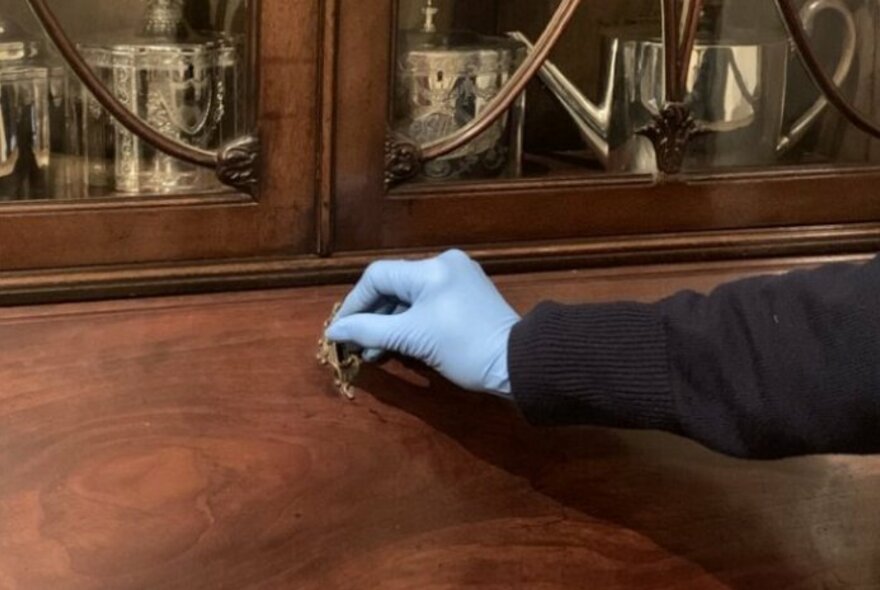 A hand wearing a blue rubber glove locking an antique wooden cabinet.