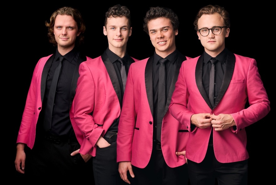 Four men in identical pink jackets and black shirts pose for a group picture against a black background. 