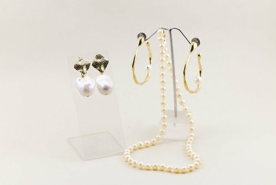 Gold and pearl earrings and necklace on display stands. 