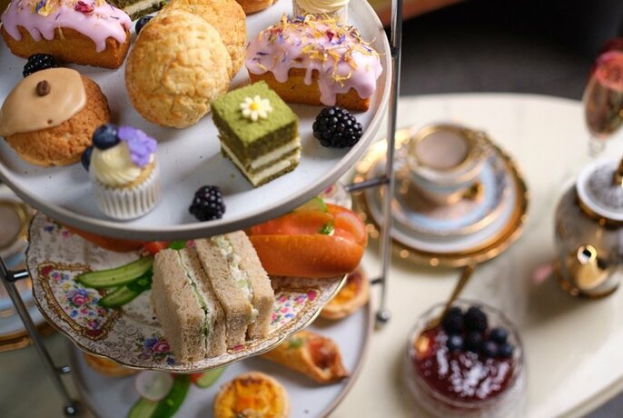 Overhead view of a High Tea spread out on a marble table, including a three-tiered tray of sweet and savoury snacks, a tea pot and cup and saucer.