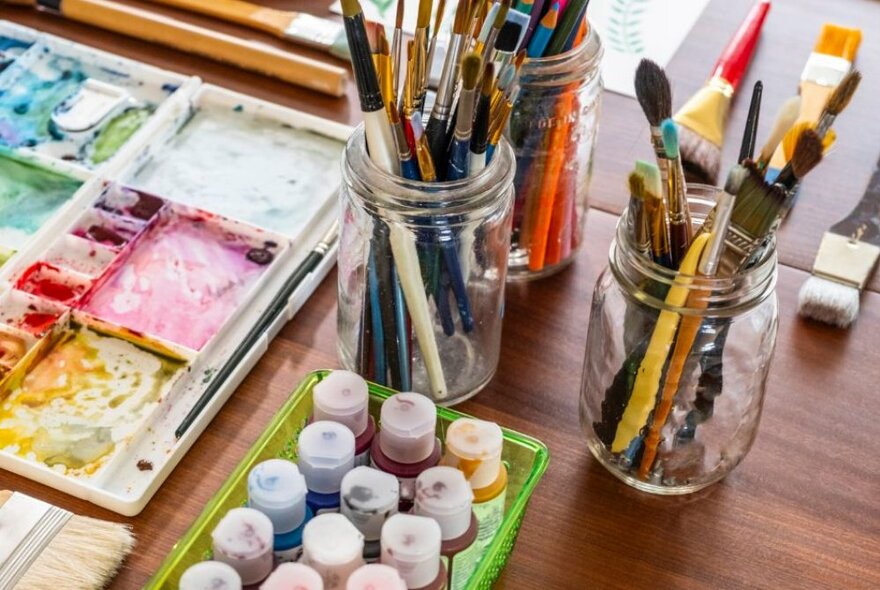 A selection of art materials including paints, jars of brushes and palettes.