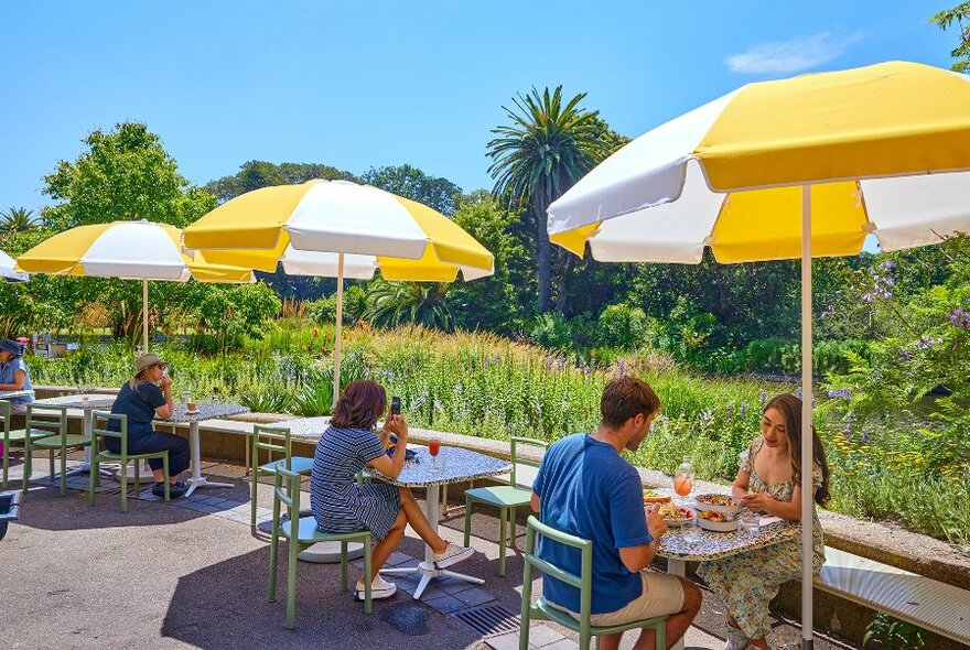 People sitting at outdoor cafe tables under yellow and white umbrellas.