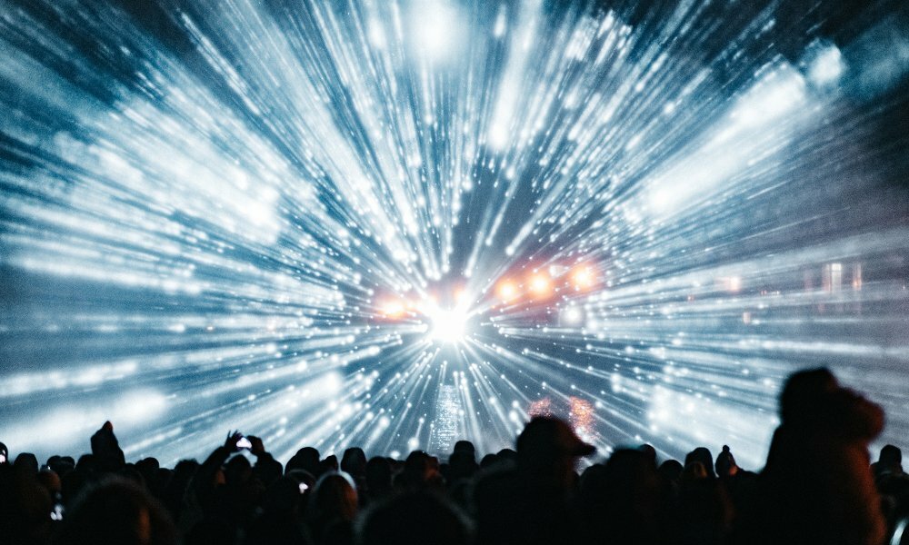 A crowd watching a light show with blue beams of light bursting out.