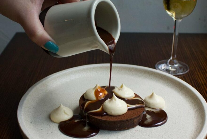 A jar of chocolate fudge being poured on a brownie.