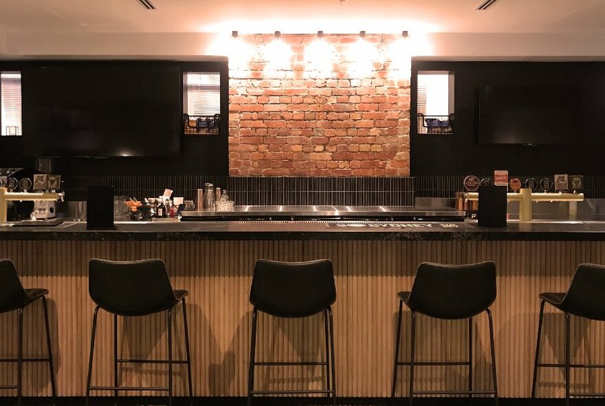A trendy timber bar with exposed bricks, dark walls and chairs and dim lighting