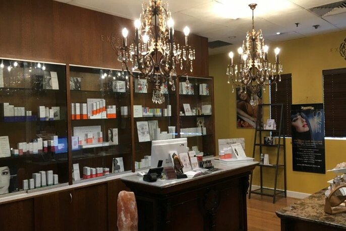 View of counter and reception area at beauty clinic showing glass shelves filled with skin products.