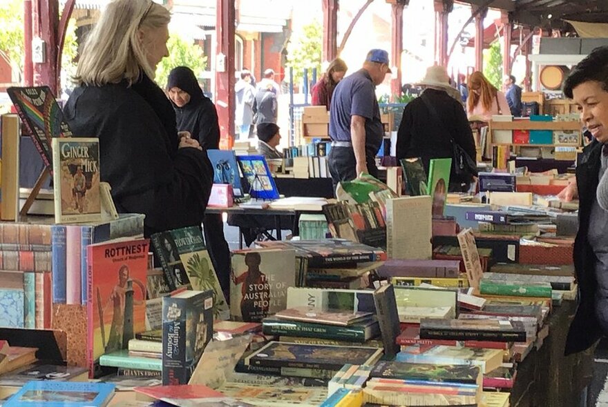 Long line of tables covered in books, with a stallholder talking to a customer.