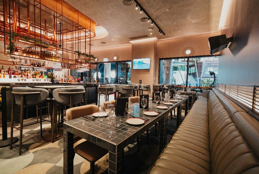 Bar space with brown banquette seating and long dining table with chairs next to bar area.