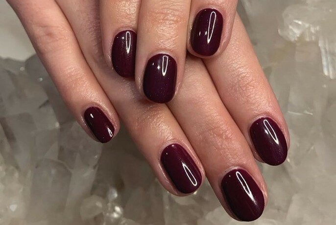 Woman's hands with glossy, dark red nail polish.