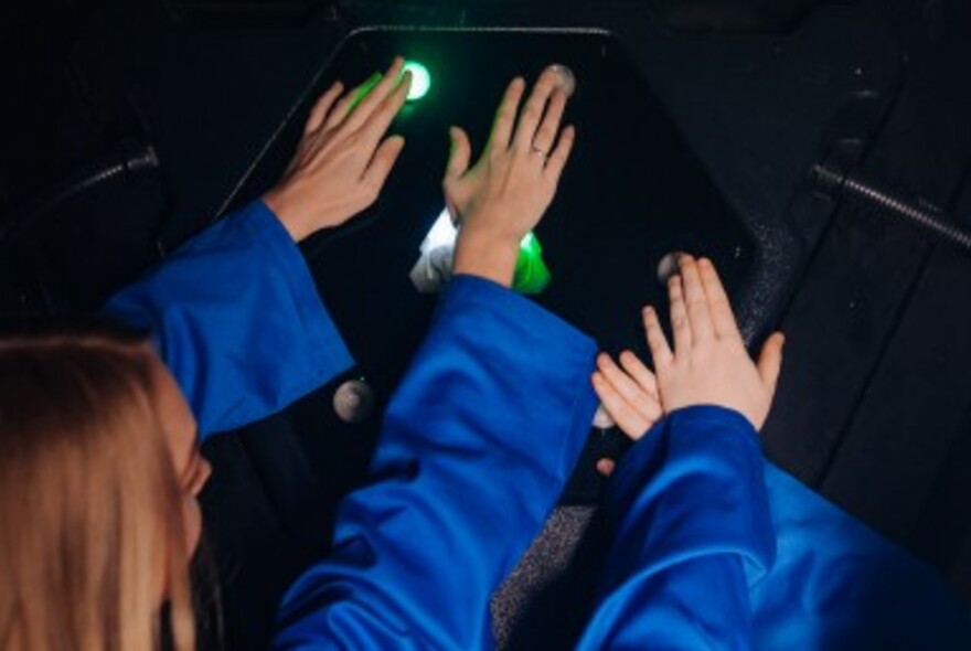 Four hands pressing lit up green buttons on a dark surface.