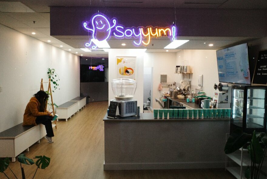 Interior of soyyum shop; serving space to right, person seated on bench against wall to left.