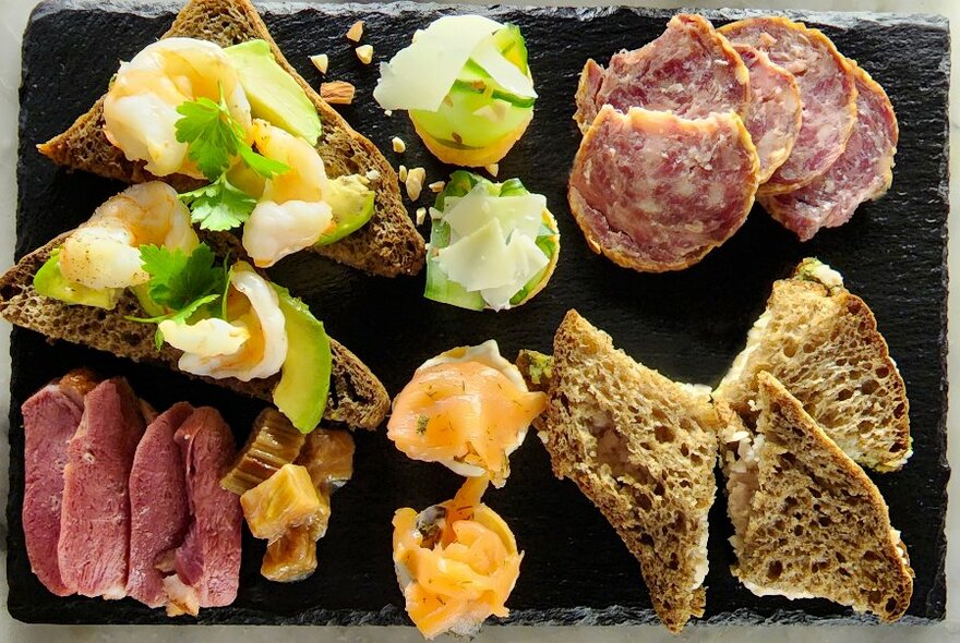 A black platter with sandwiches and meats.