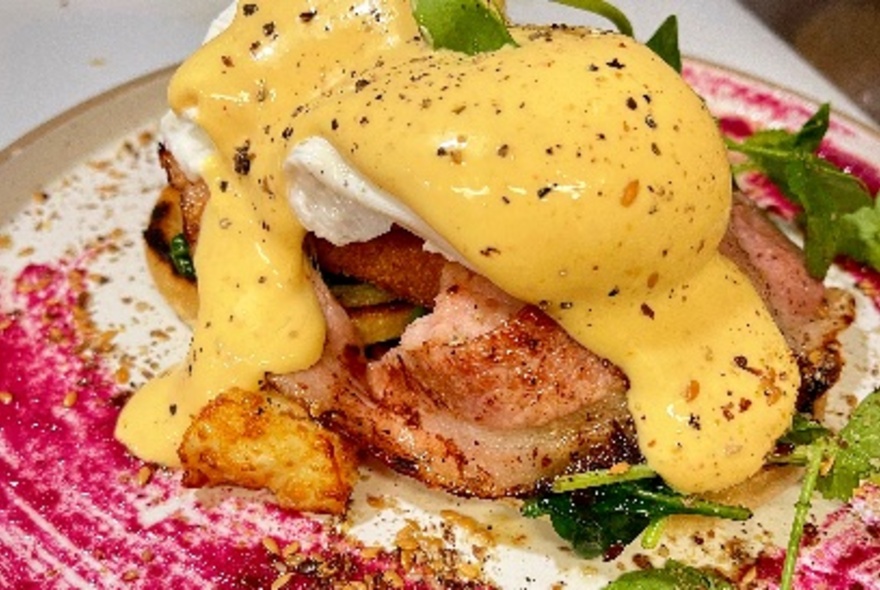 Breakfast dish of eggs Benedict topped with creamy yellow sauce.