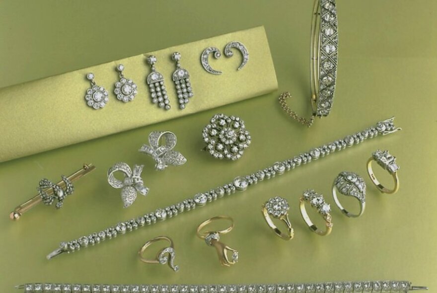Diamond and pearl jewellery resting on pale green fabric, including earrings, bracelets and rings.