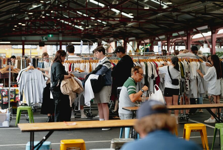 People browsing racks of clothing in a shed at Queen Victoria Market.