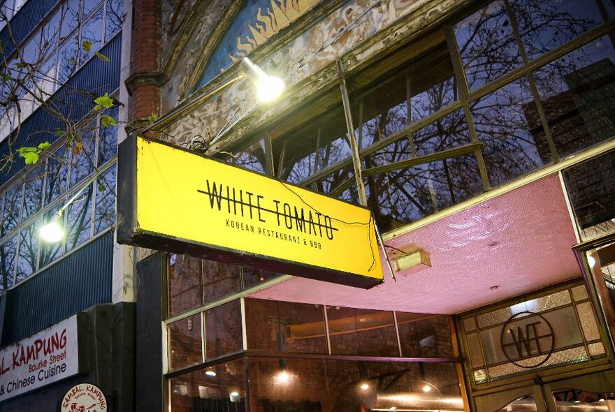 Exterior of White Tomato Korean restaurant showing restaurant entrance and yellow street signage.