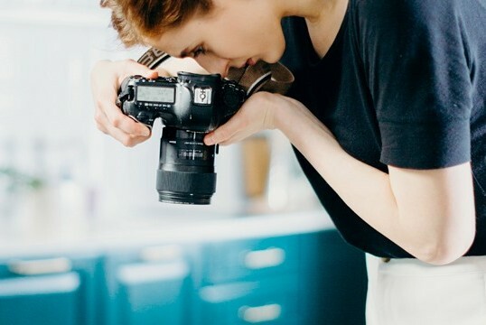 Woman holding and looking through an SLR camera.