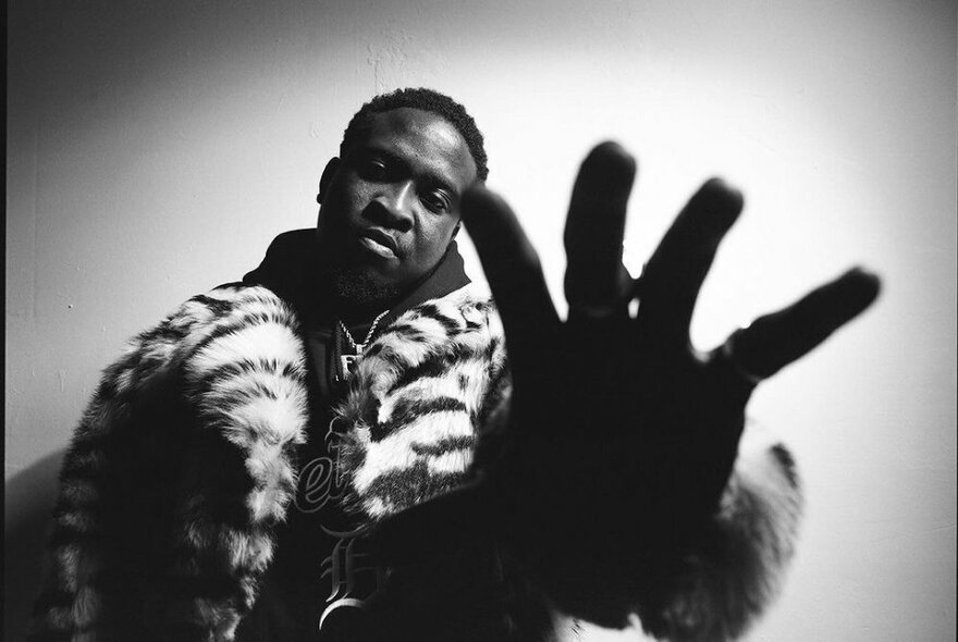 Black and white shot of English musician, Kojo Funds wearing a zebra-print fur coat and reaching out towards the camera.