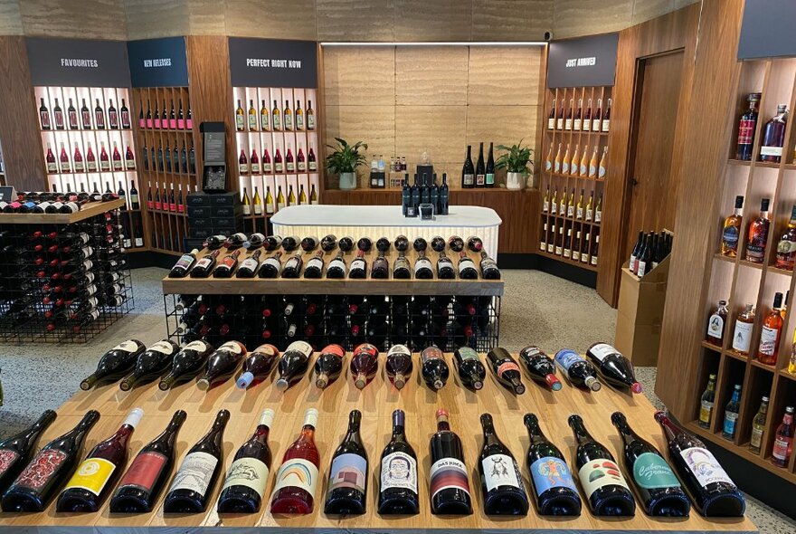 The interior of a wine store with bottles of wine displayed on wooden shelves and benches.