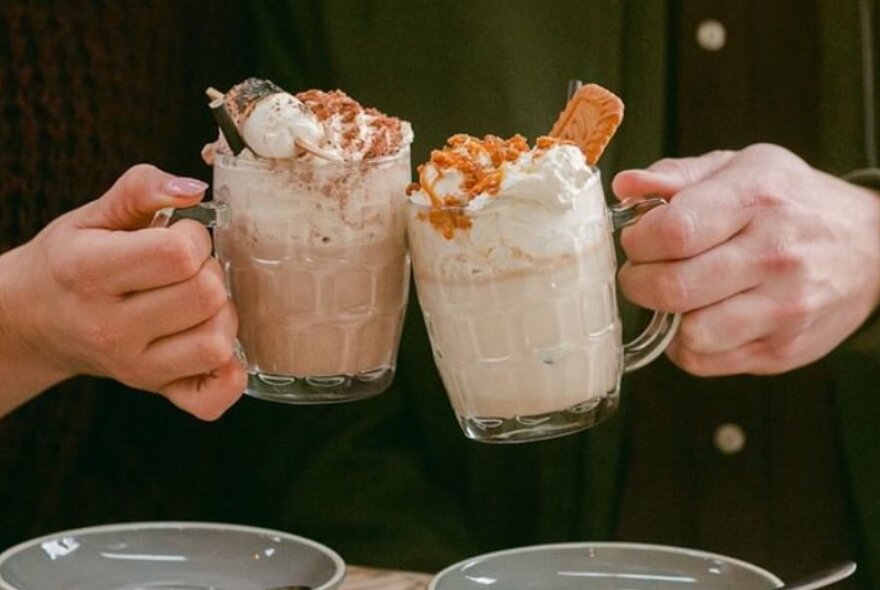 Two people raising glasses filled with milky cocktails topped with cream. 