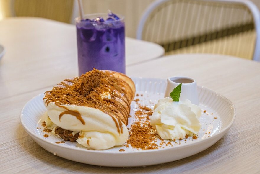 A souffle pancake with Biscoff crumbs and cream, with a purple iced latte. 