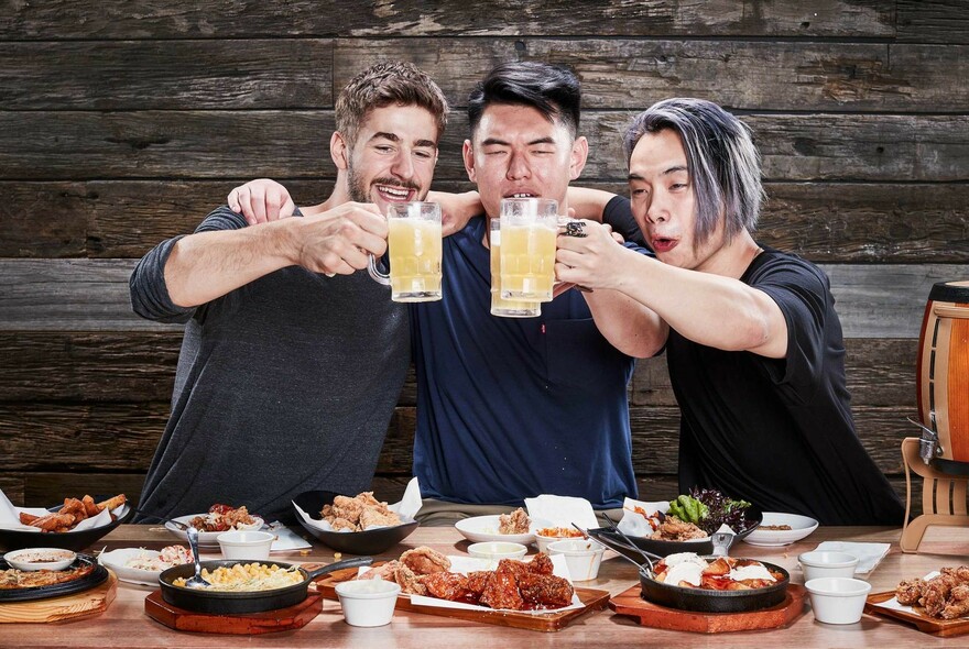 Three people holding beers and enjoying a Korean food.
