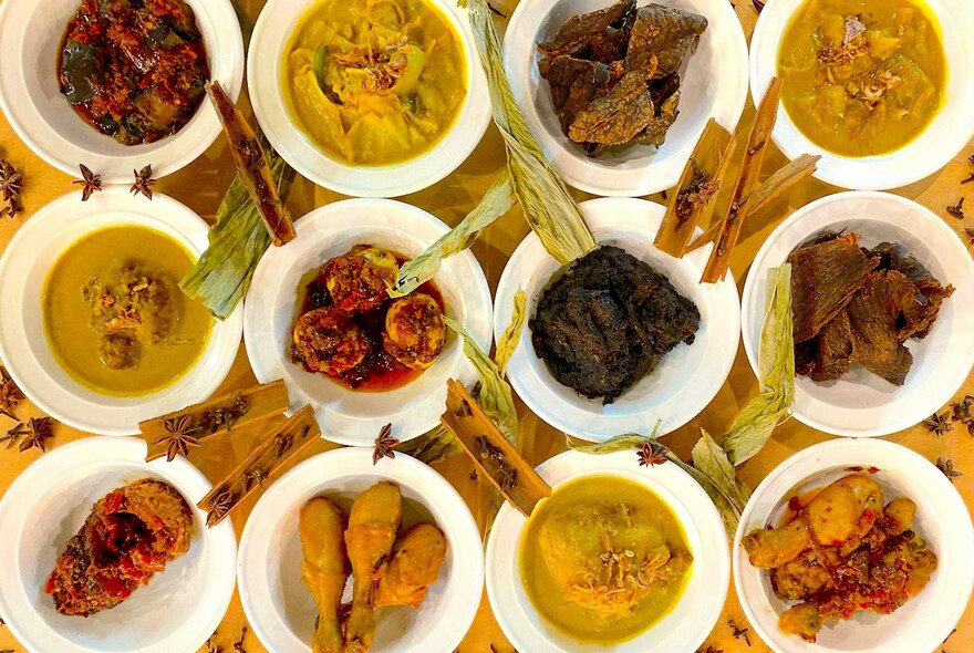 Rows of white dishes with yellow and red soups, curries and meat.