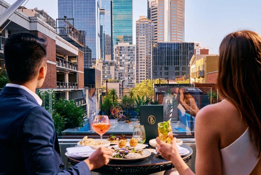 A couple sharing a bit to eat and cocktails looking at the city skyline. 