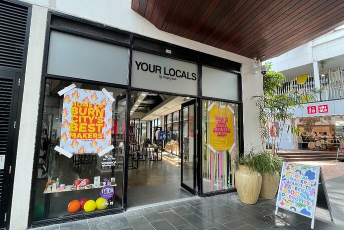 Exterior of the shop Your Locals in Docklands showing paved entrance and large glass windows and door.