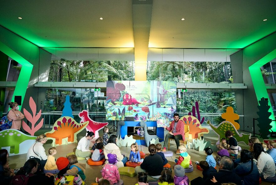 Young children seated on the floor in a museum setting, surrounded by dinosaur-themed cutouts.