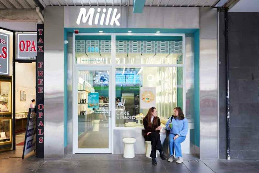 Two women sipping coffee outside a cake shop 