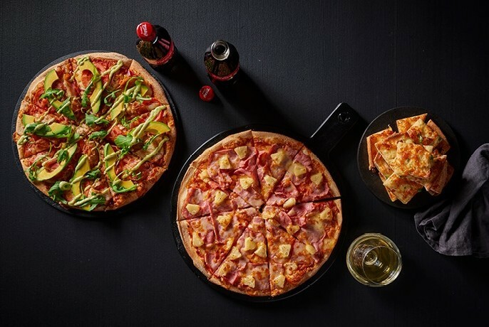 Two pizzas and small bottles of soft drink seen from above, on a black table.
