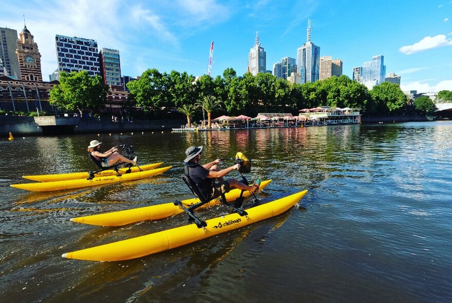Two yellow water bikes on Yarra, cityscape at rear.