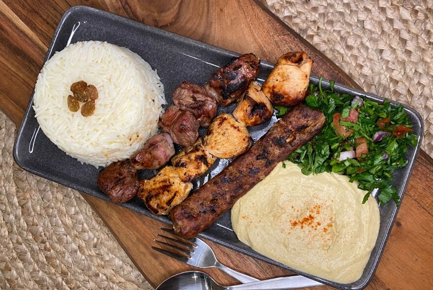 A platter of food that includes rice, meat skewers, a dip and salads.